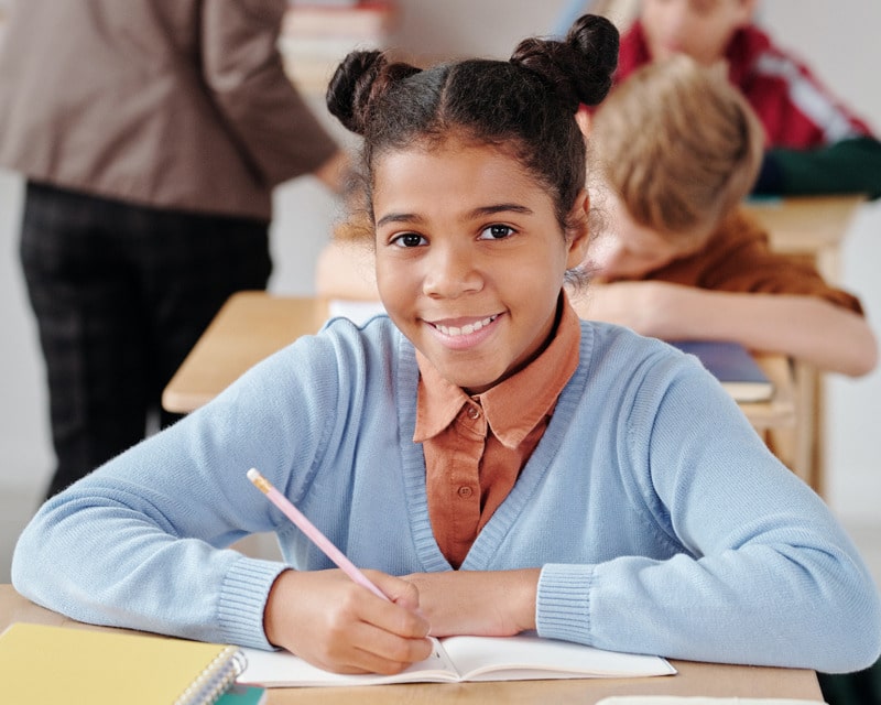 girl holding a pencil and smiling in a classroom