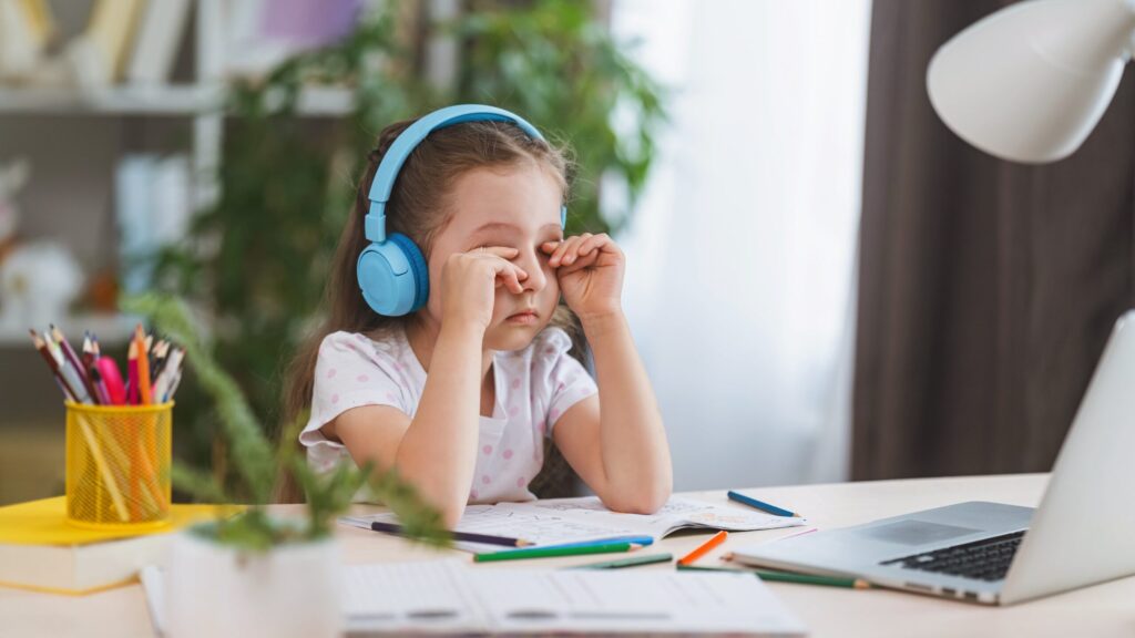 young girl with headphones on rubbing her eyes