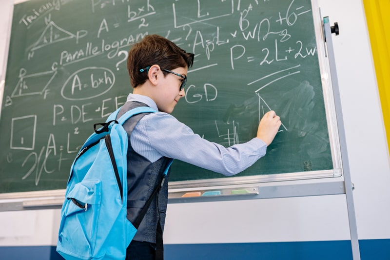 young boy solving a math problem on a chalkboard