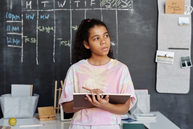 girl with notebook thinking in front of chalkboard